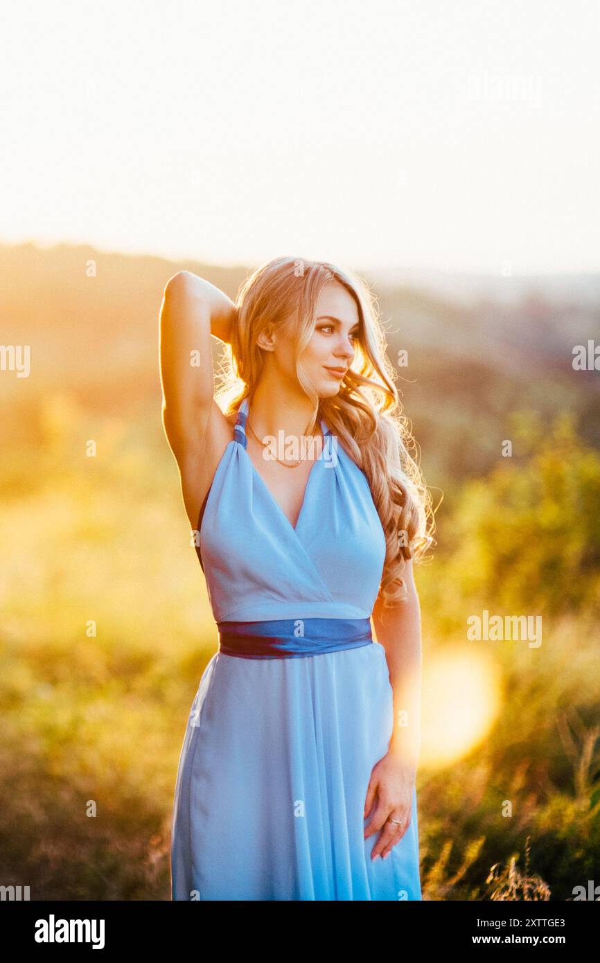 Blonde mit lockeren Haaren in einem hellblauen Kleid in Das Licht des Sonnenuntergangs in der Natur Stockfoto