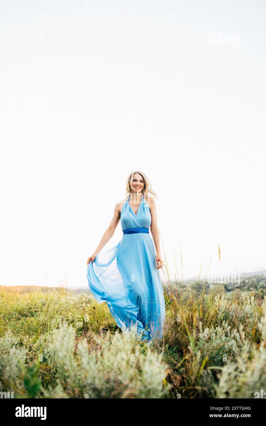 Blonde mit lockeren Haaren in einem hellblauen Kleid in Das Licht des Sonnenuntergangs in der Natur Stockfoto