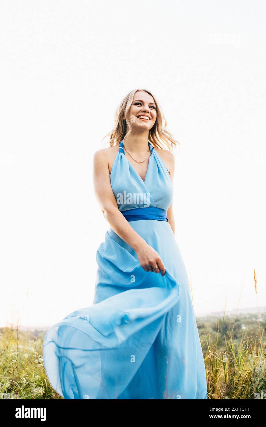 Blonde mit lockeren Haaren in einem hellblauen Kleid in Das Licht des Sonnenuntergangs in der Natur Stockfoto