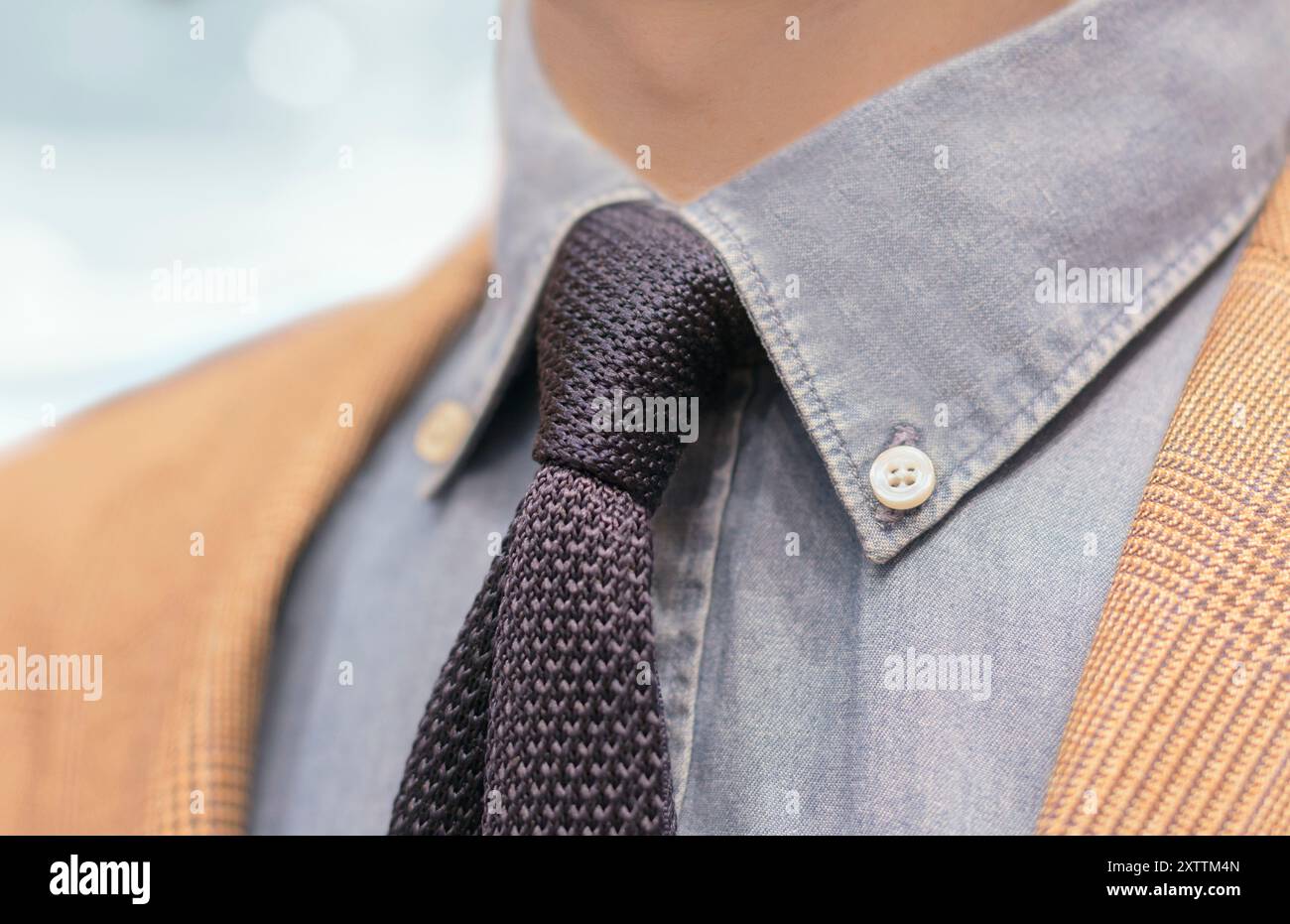 Anonymer Mann in stilvoller, eleganter Freizeitkleidung mit blauem Hintergrund. Das Outfit besteht aus einer beigefarbenen Jacke mit blauem Hemd und gestrickter Krawatte. Stockfoto