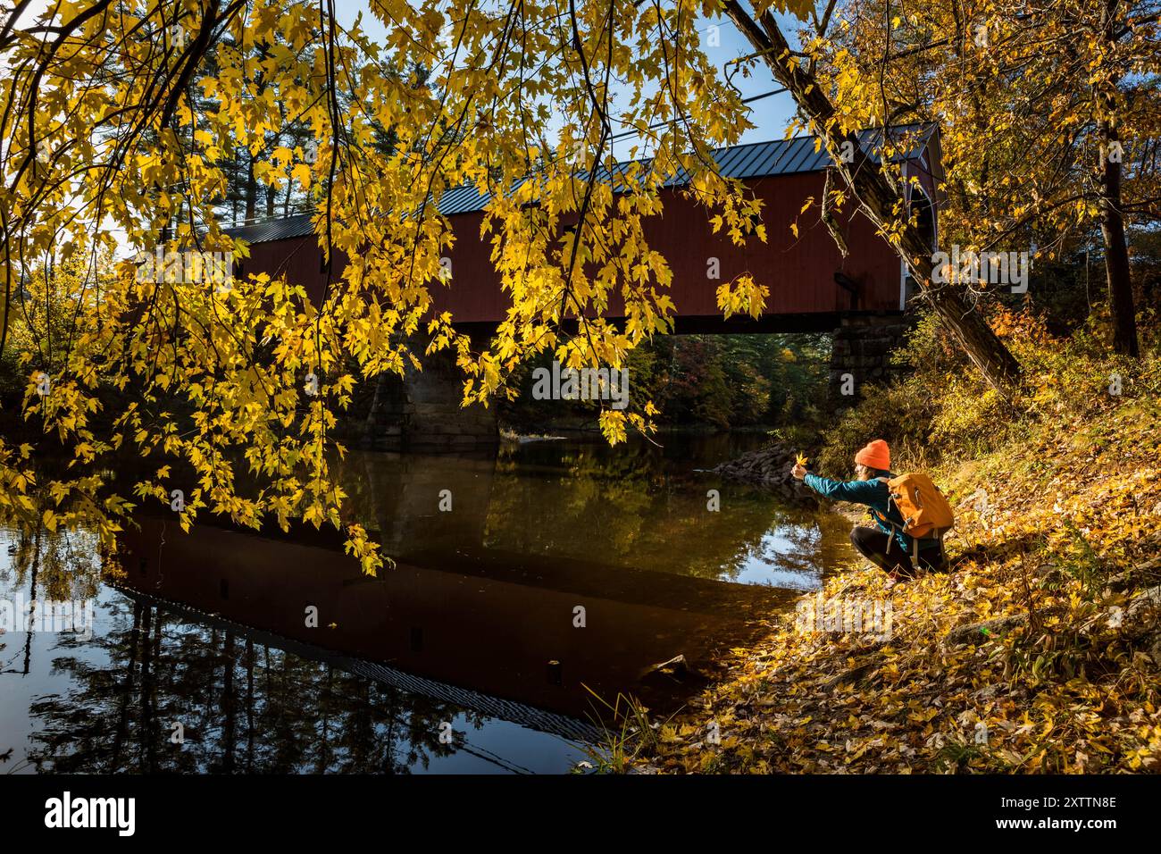 Frau mit Ahornblatt umgeben von Herbstlaub Stockfoto