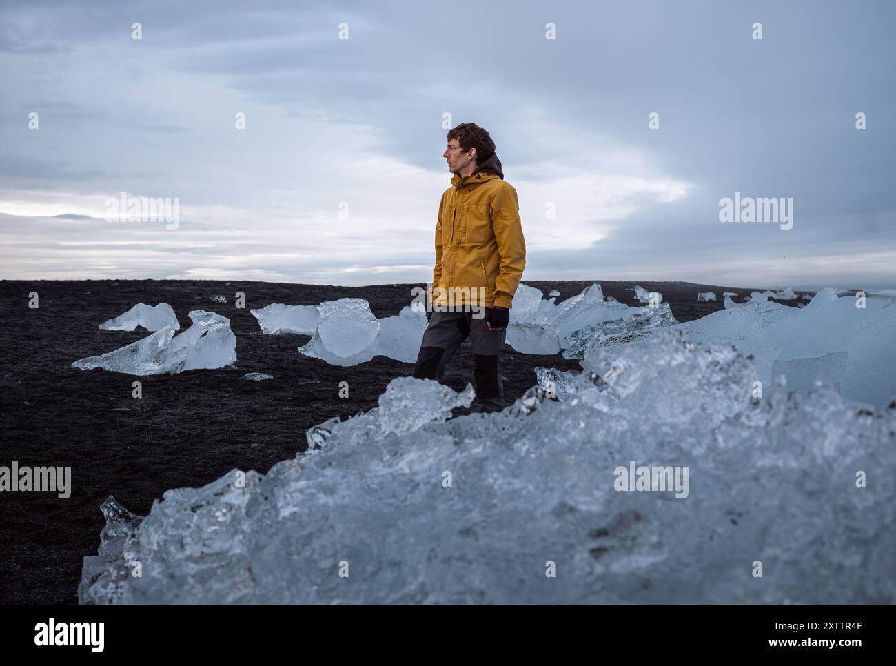 Ein junger Mann in gelber Jacke steht am Diamond Beach, Island Stockfoto