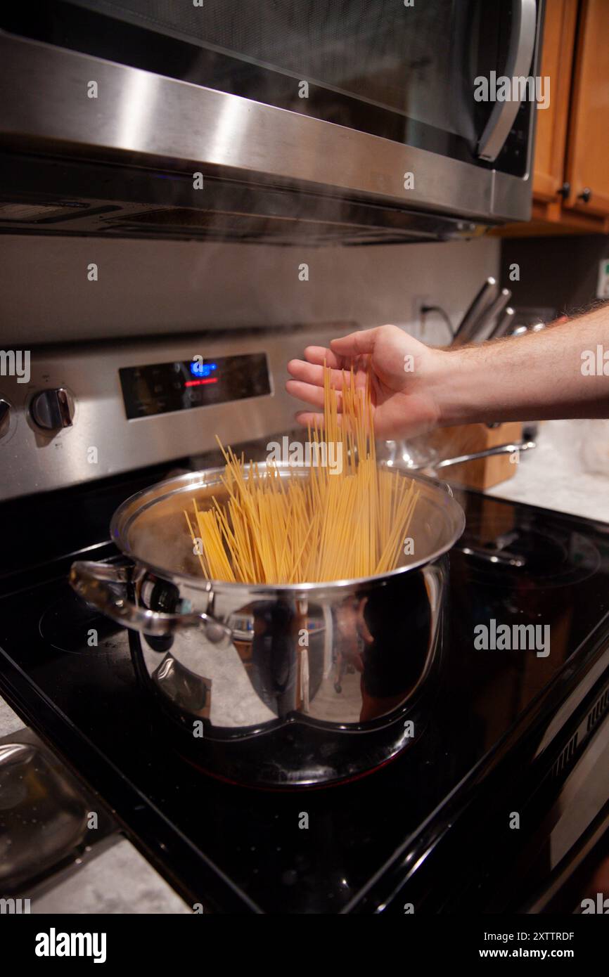 Ungekochte Spaghetti, die in einen Topf mit kochendem Wasser auf dem Herd gehen Stockfoto