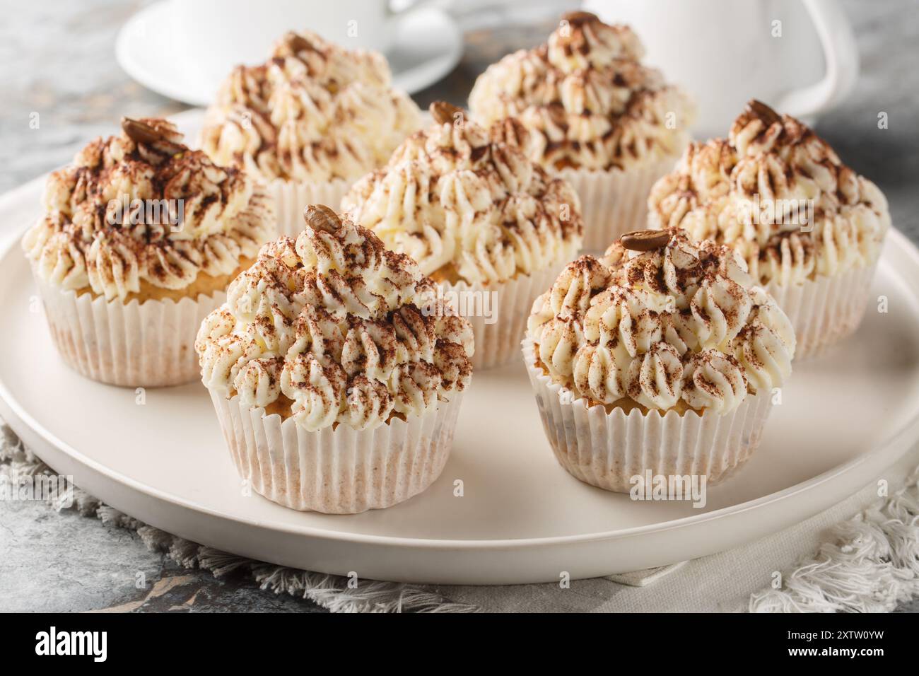 Delikate Tiramisu Cupcakes mit cremiger Mascarponcreme und Kakao serviert mit Kaffee in Nahaufnahme auf einem Teller auf einem Tisch. Horizontal Stockfoto