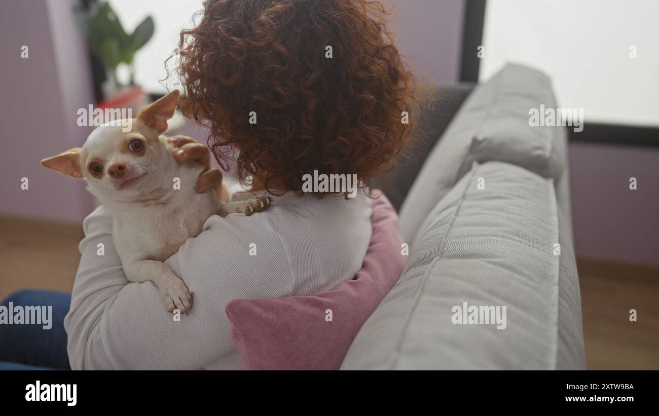 Eine Frau mittleren Alters hält ihren chihuahua in einem gemütlichen Wohnzimmer und schafft so einen warmen und liebevollen Moment zu Hause. Stockfoto