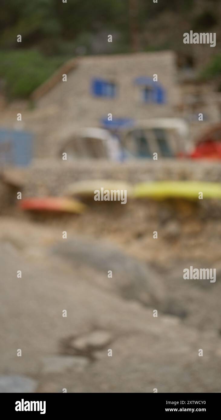 Verschwommener Hintergrund mit Kajaks und rustikalen Gebäuden mit blauen Fenstern in cala deia, mallorca, die eine Küstenszene im Freien mit einem Out-o veranschaulichen Stockfoto