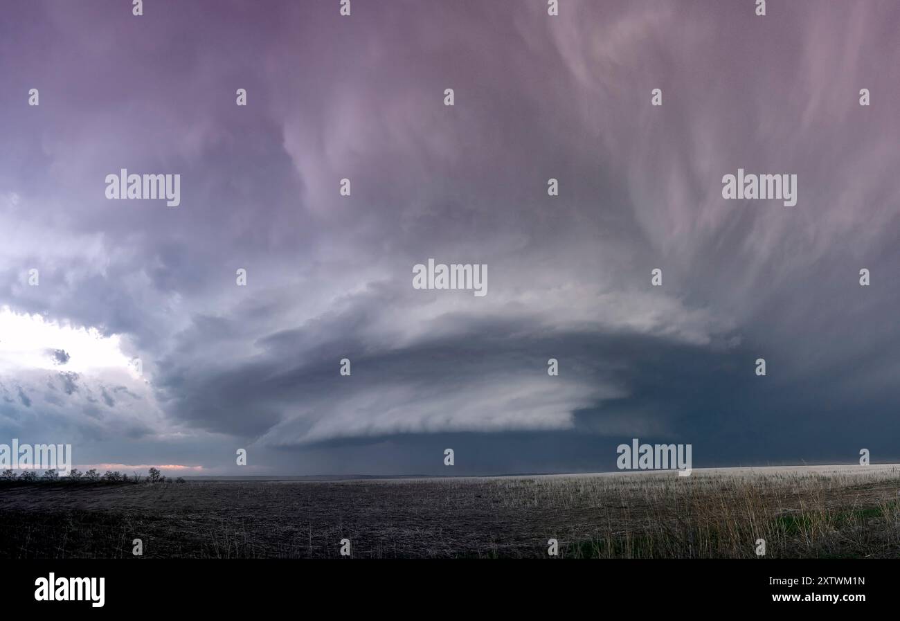 Dramatische Sturmwolken über einem weitläufigen Feld in der Abenddämmerung mit einem Blick auf das Sonnenlicht am Horizont. Stockfoto