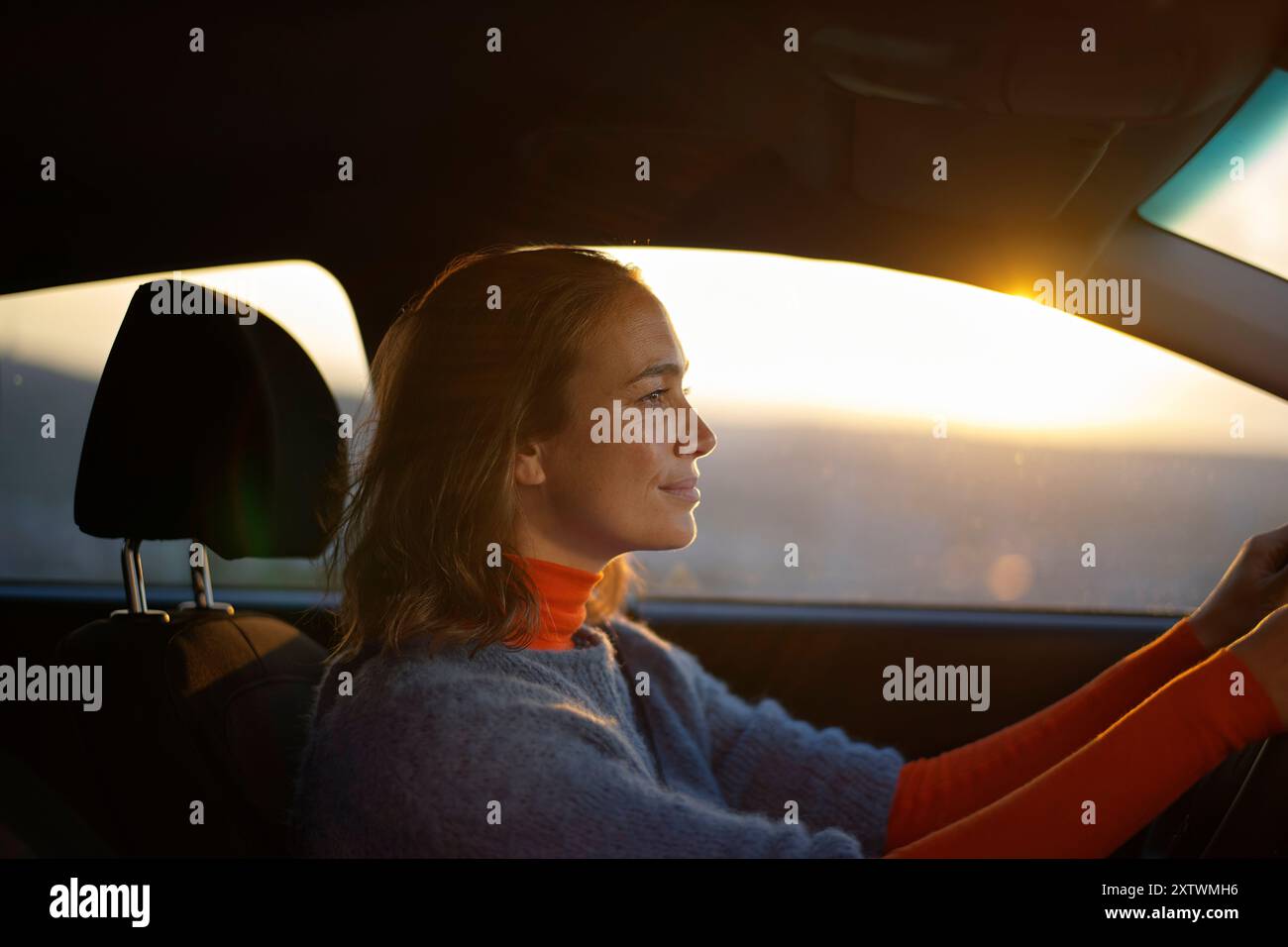 Frau, die bei Sonnenuntergang Auto fährt, mit warmem Licht im Gesicht. Stockfoto