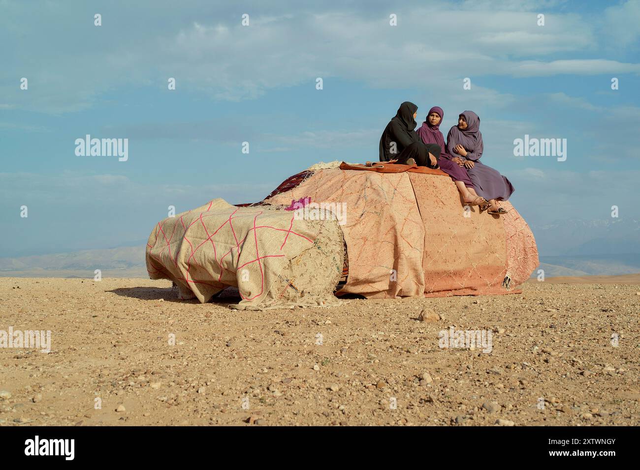 Frauen in traditioneller Kleidung sitzen auf einem mit Stoff bedeckten Gebäude in einer Wüstenlandschaft, unter einem klaren blauen Himmel. Stockfoto