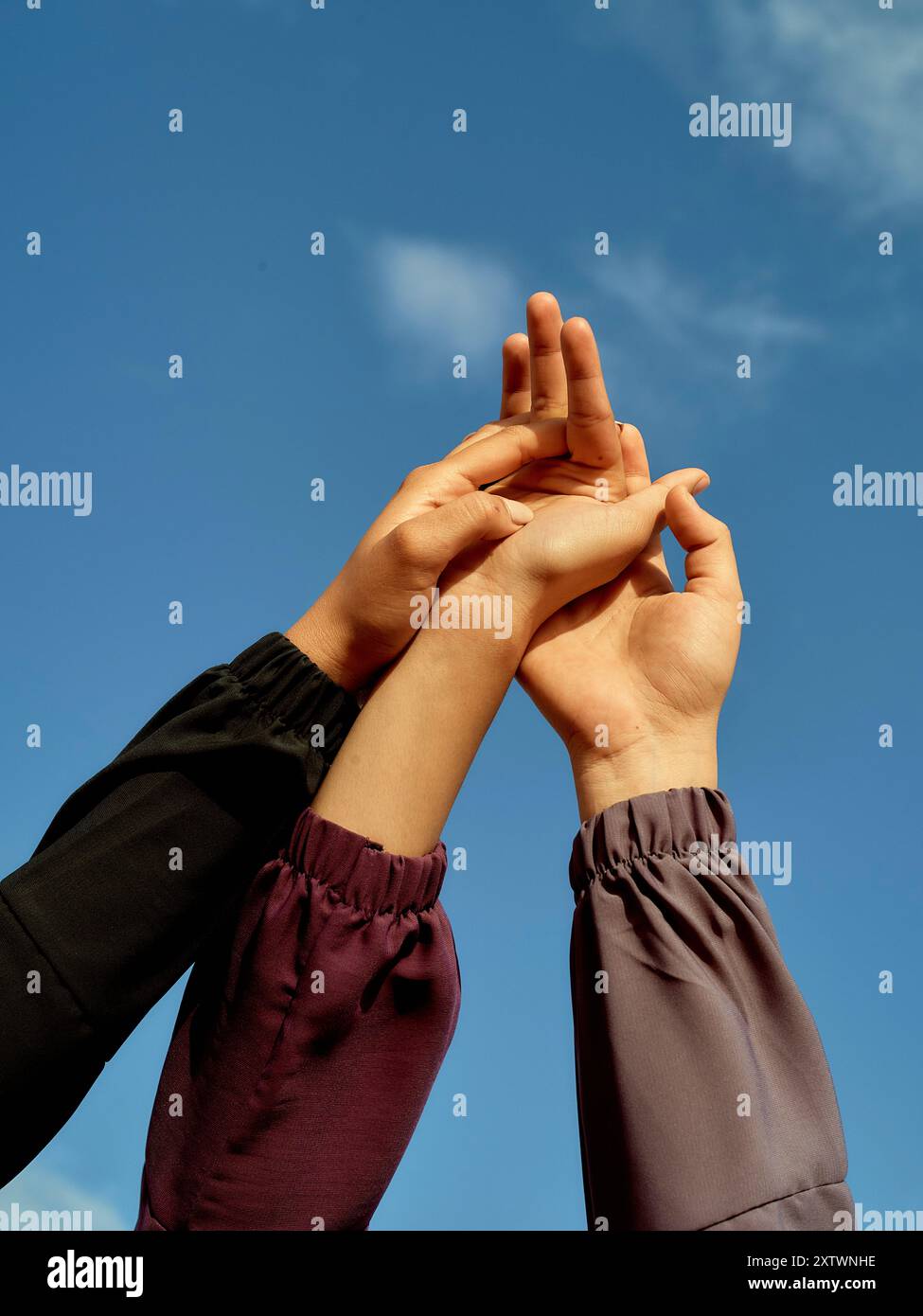 Die Hände greifen in Richtung eines klaren blauen Himmels, wobei die Finger die Spitzen in einer Geste der Verbindung berühren. Stockfoto