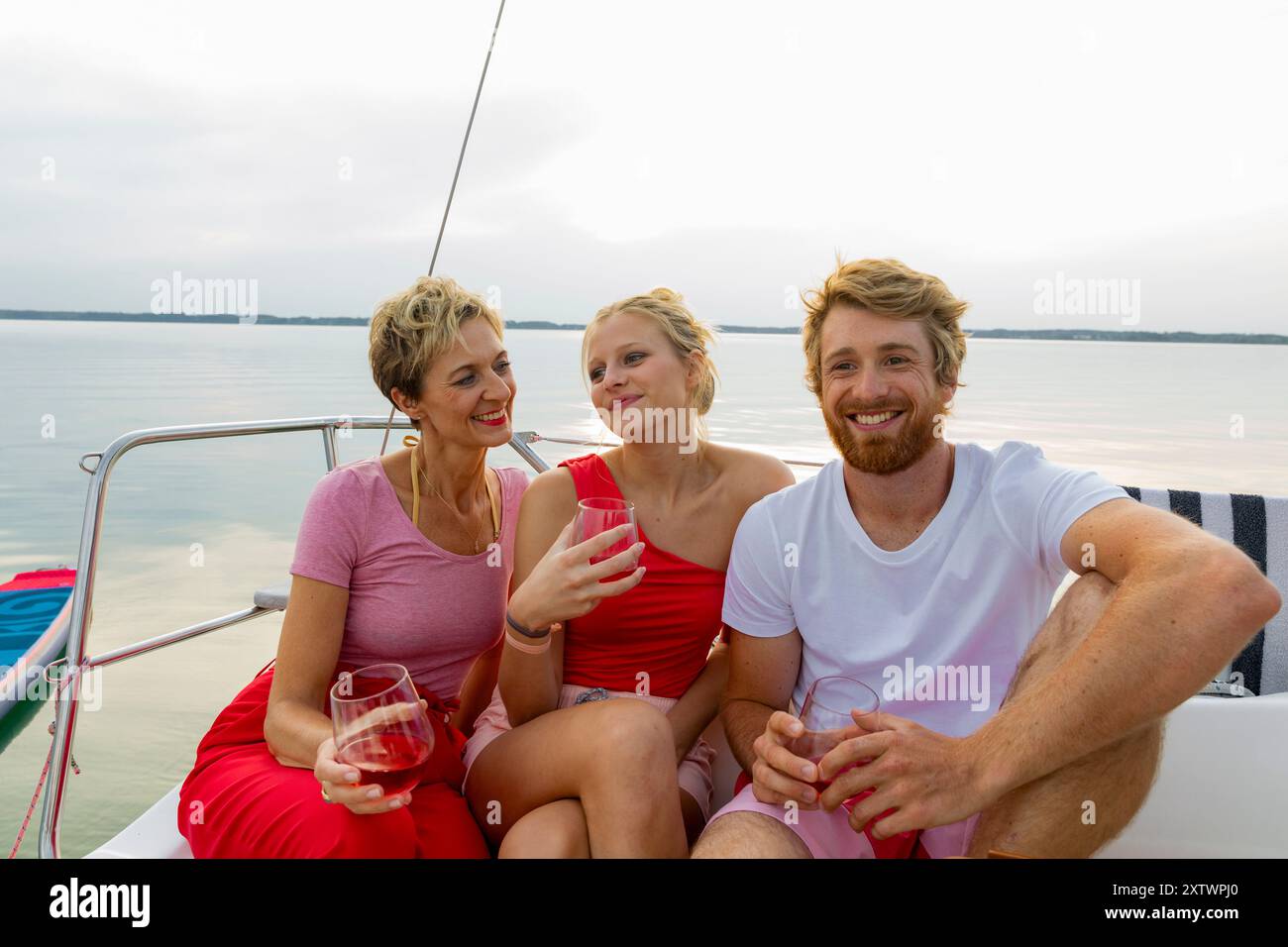 Drei Freunde genießen Drinks, während sie in der Abenddämmerung auf einem Segelboot entspannen. Stockfoto