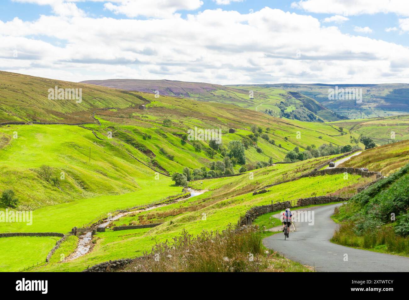 Stonesdale Lane, Swaledale, Yorkshire Dales, Großbritannien im Sommer, mit hohen Fjells, Moor, River Swale und Trockenmauern sowie Radfahrer und Autofahrer Stockfoto