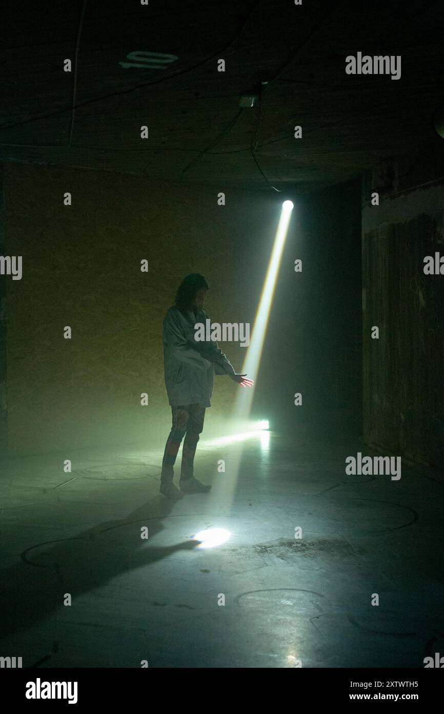 Eine Person mit Silhouette, die in einem dunklen Raum steht und von einem starken Lichtstrahl aus einer Öffnung beleuchtet wird. Stockfoto