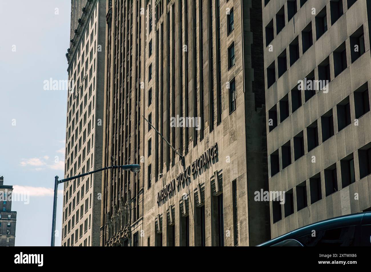 Sonnenlicht reflektiert die Fassade des New Yorker Börsengebäudes, flankiert von anderen Hochhäusern unter einem klaren blauen Himmel. Stockfoto