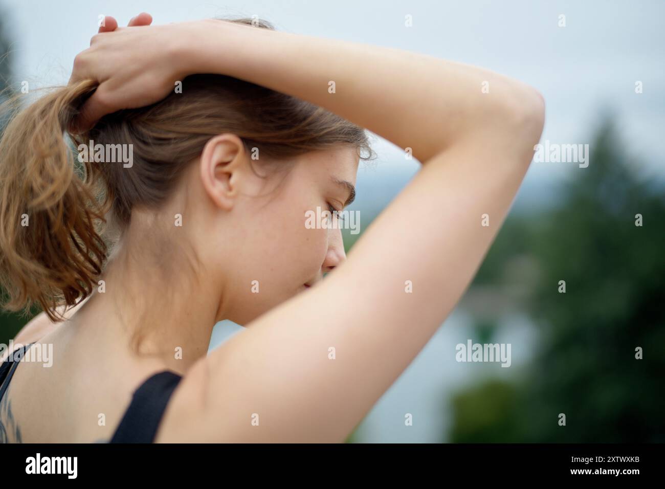 Nahaufnahme einer jungen Frau, die ihr Haar in einer natürlichen Umgebung im Freien bindet. Stockfoto