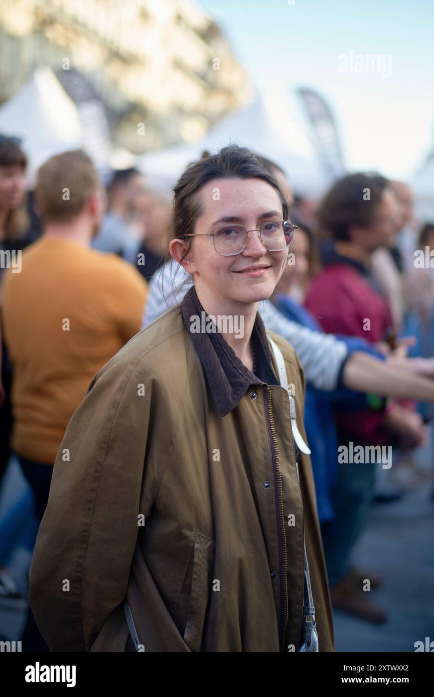 Lächelnde Frau, die eine Brille trägt, mit einer Menge im Hintergrund während einer Veranstaltung im Freien. Stockfoto