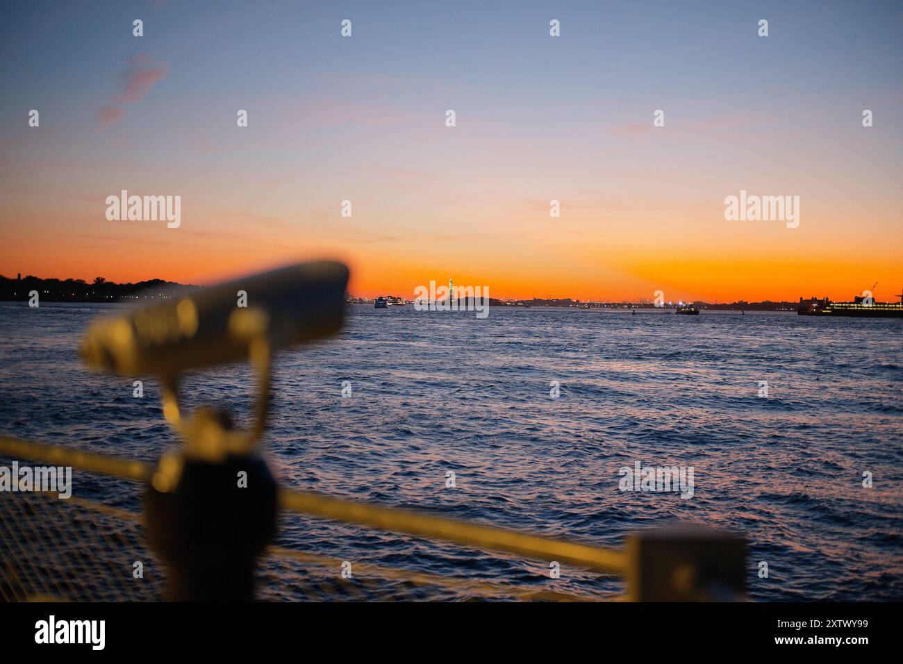 Blick auf den Sonnenuntergang über dem Wasser mit einem Teleskop im Vordergrund vor einem lebendigen Himmel. Stockfoto