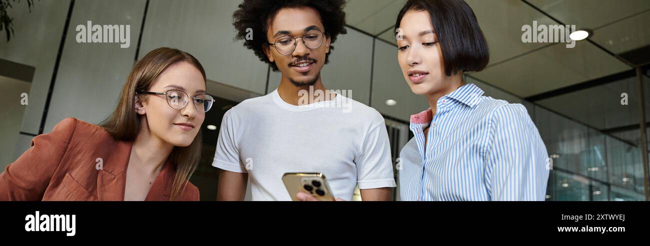 Drei Kollegen treffen sich in der Lobby des Büros und besprechen etwas auf einem Smartphone. Stockfoto
