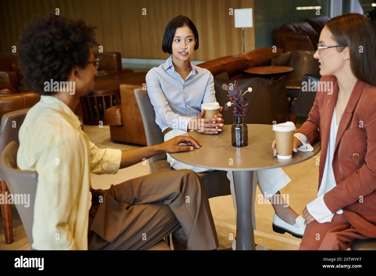 Drei Kollegen versammeln sich an einem Tisch in einem modernen Büro, genießen Kaffee und Gespräche. Stockfoto