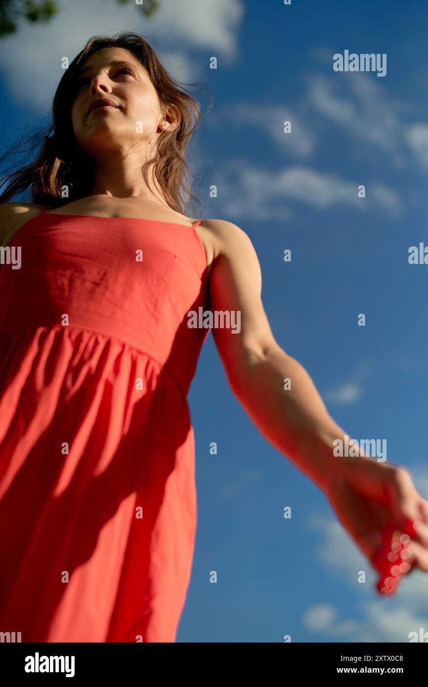 Frau in rotem Kleid, die unter blauem Himmel mit Wolken steht. Stockfoto