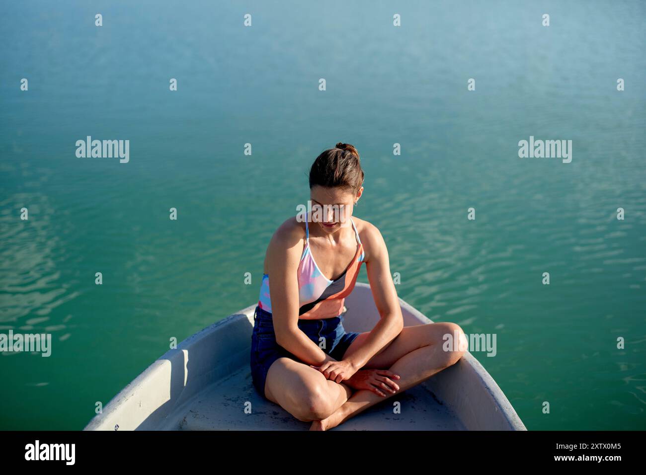 Frau, die im Kreuz in einem Boot auf einem ruhigen See sitzt, tief in Gedanken. Stockfoto