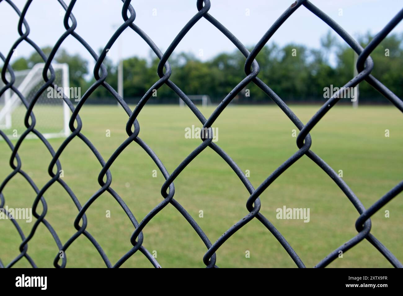 Blick durch den Maschendrahtzaun auf das grüne Feld mit besseren Zielen Stockfoto