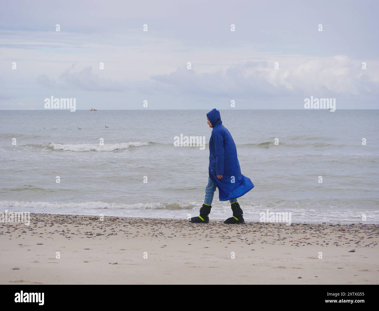 Ein Mann mit blauem Regenmantel und wasserdichten Stiefeln, der am Strand Grenen in Skagen entlang geht. Stockfoto