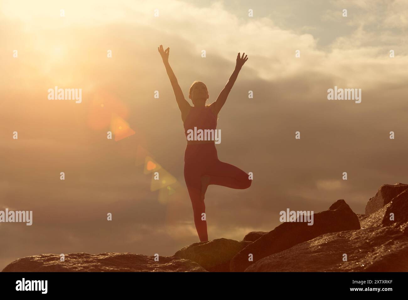 Frau, die einen Baum macht, posiert Yoga-Position draußen auf Felsen bei Sonnenaufgang und Sonnenuntergang. Stockfoto