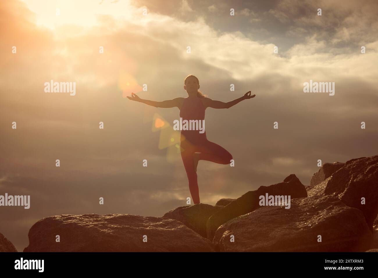 Frau, die einen Baum macht, posiert Yoga-Position draußen auf Felsen bei Sonnenaufgang und Sonnenuntergang. Stockfoto
