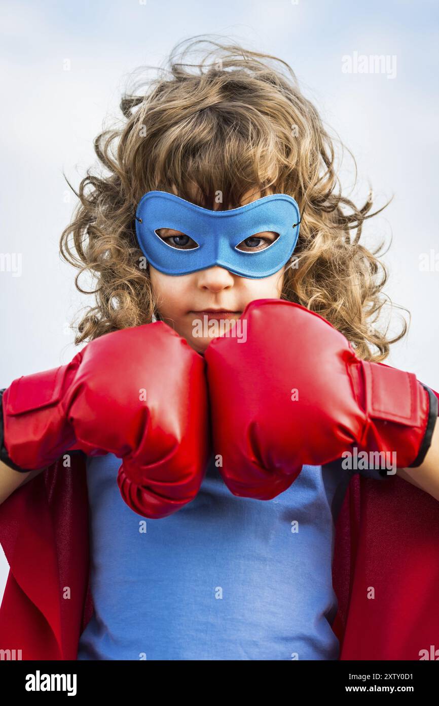 Superheldenkind mit Boxhandschuhen vor blauem Himmel. Mädchenmacht und Feminismuskonzept Stockfoto