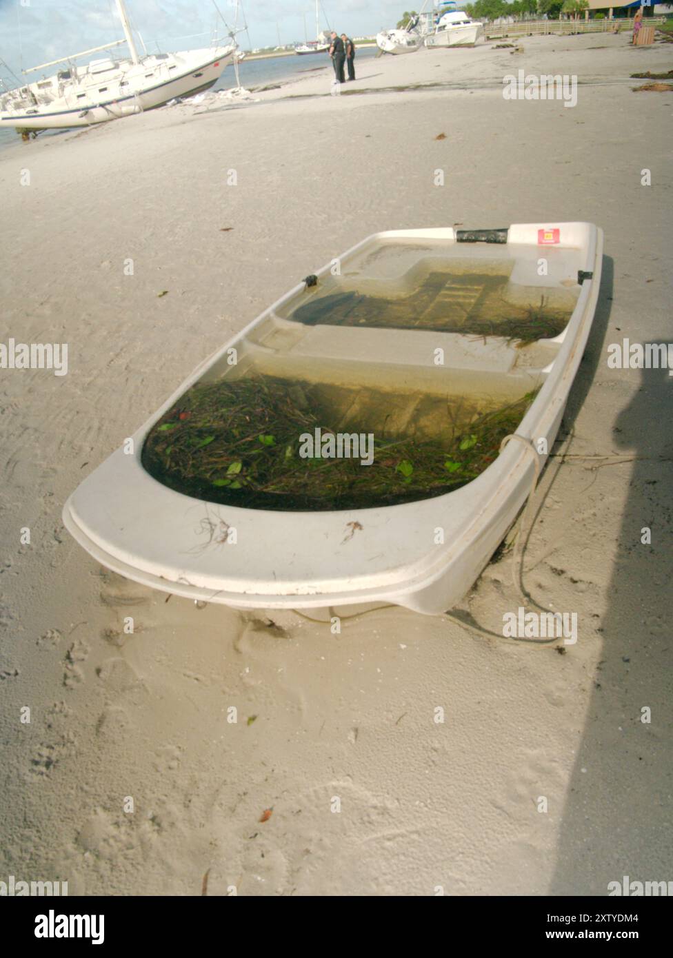 Kleines weißes Ruderboot gefüllt mit Wasser, das nach einem großen Sturm am Ufer lag. Gulfport Florida mit dem Strand und dem blauen Himmel im Hintergrund. Ein Stockfoto