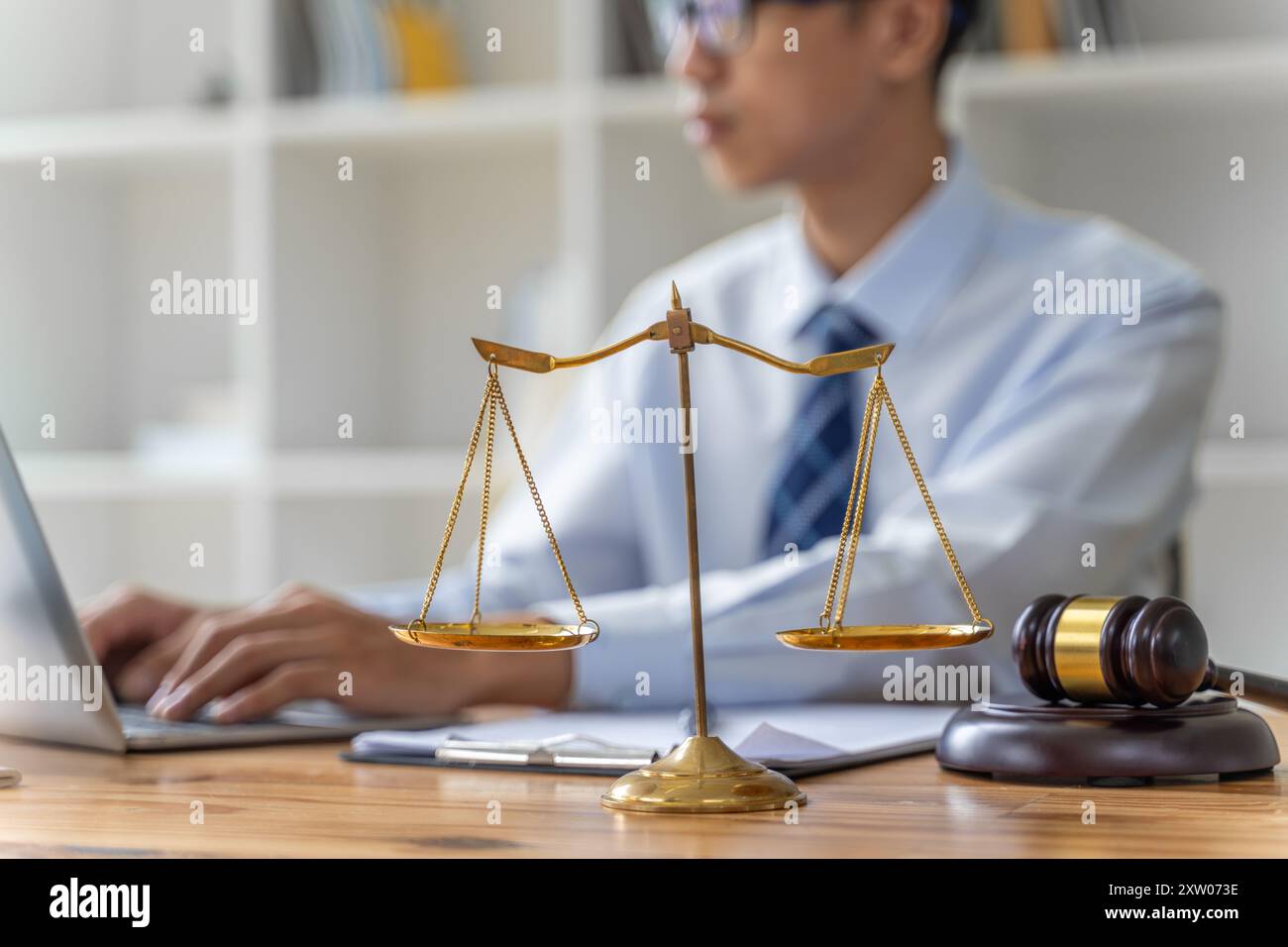 Nahaufnahme der Justizskala und des Gerichtsbeschabels mit verschwommenem arbeitendem männlichen Anwalt im Hintergrund Stockfoto