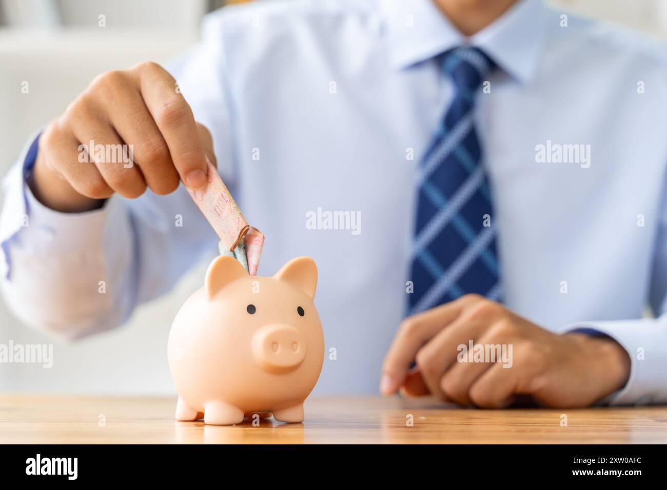 Nahaufnahme eines Geschäftsmannes, der ein Mond in eine rosa Sparkasse legt, mit einem kleinen Hausmodell auf dem Tisch, Sparen oder Hypothekenkonzept Stockfoto