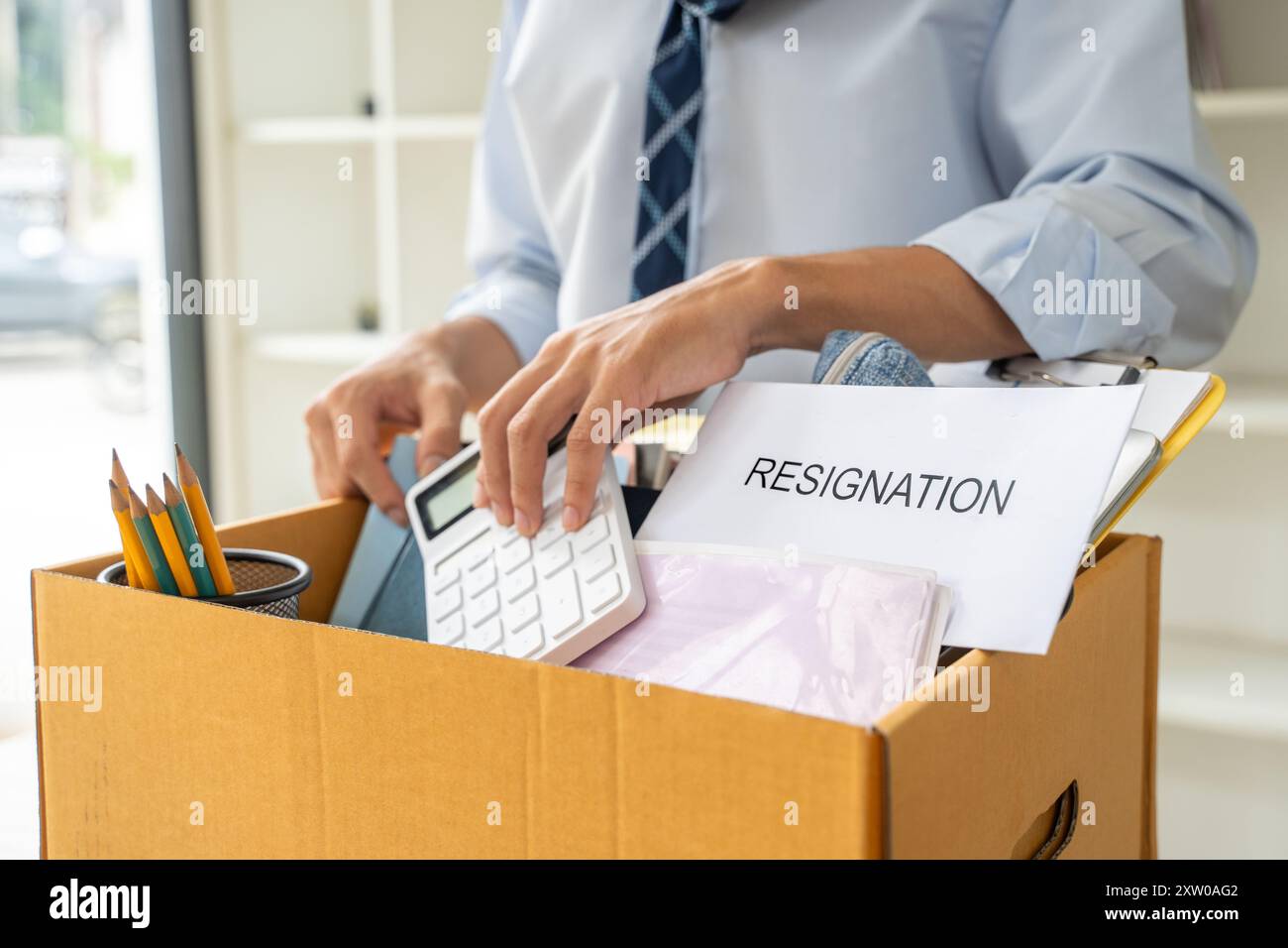 Trauriger junger Geschäftsmann, der seine Sachen in eine Kiste packt, bevor er sein Büro nach seinem Rücktritt verlässt Stockfoto