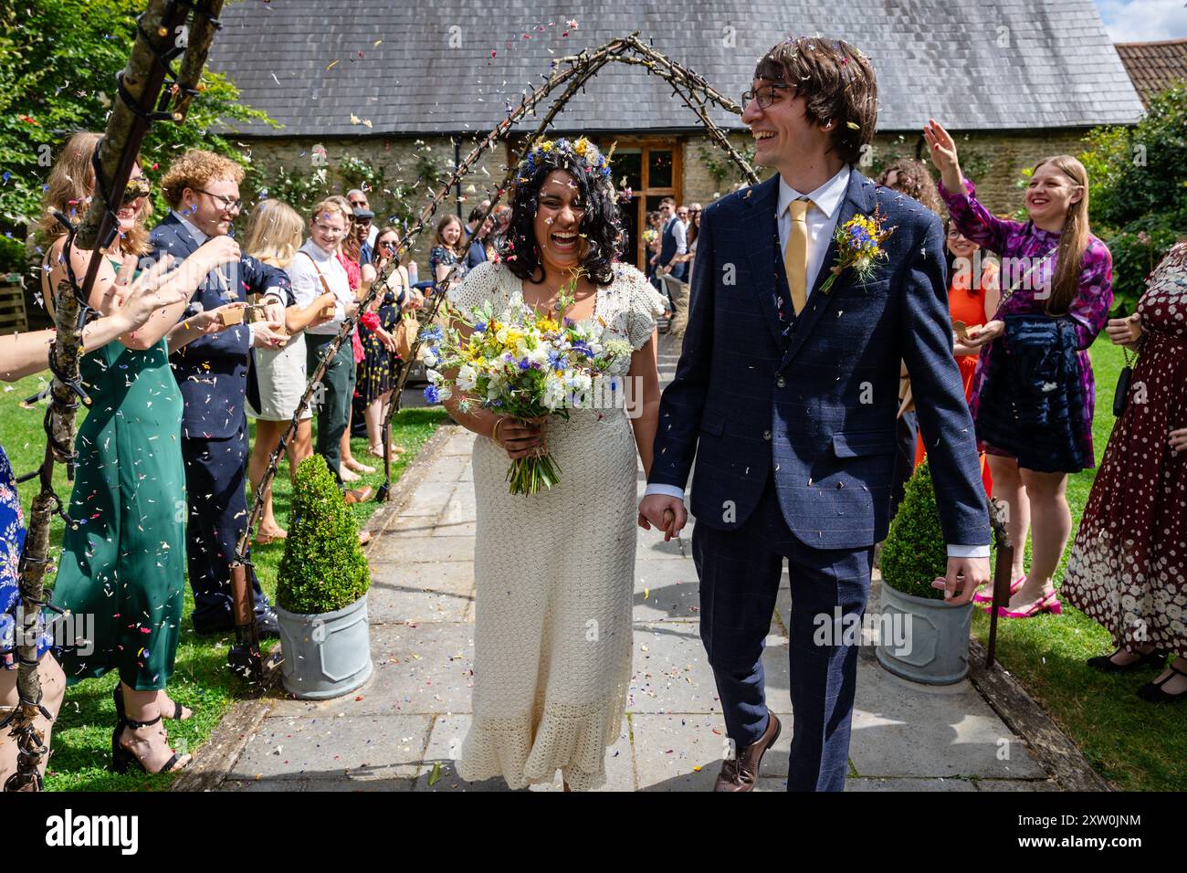 Braut und Bräutigam gehen von der Hochzeitszeremonie aus, während die Gäste Konfetti werfen. Stockfoto