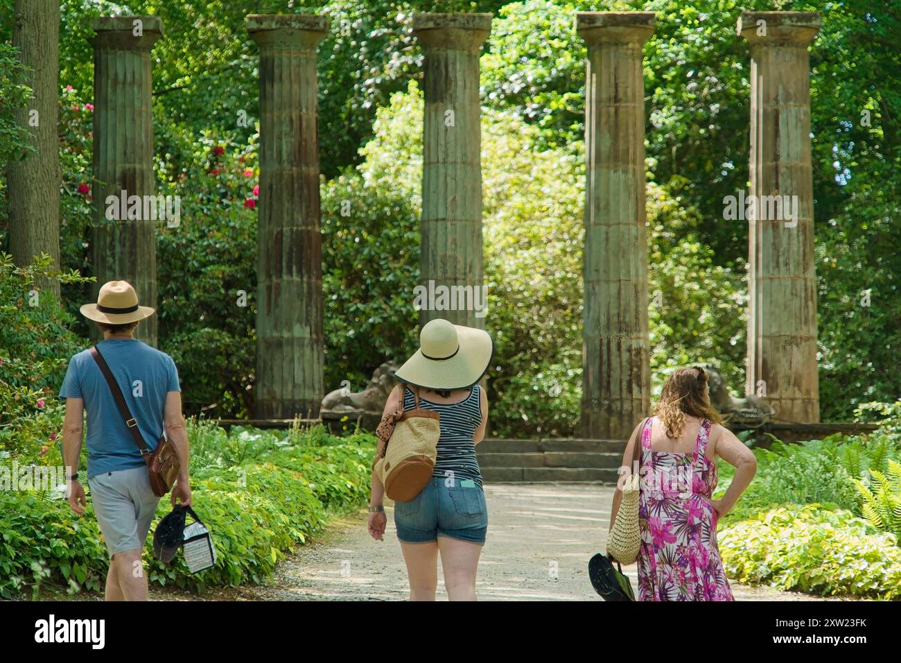 Drei Touristen erkunden die Ruinen der dorischen Steinsäule in R.H.S. Gardens, Harlow Carr, Harrogate, Yorkshire, Großbritannien, umgeben von Grün. Stockfoto