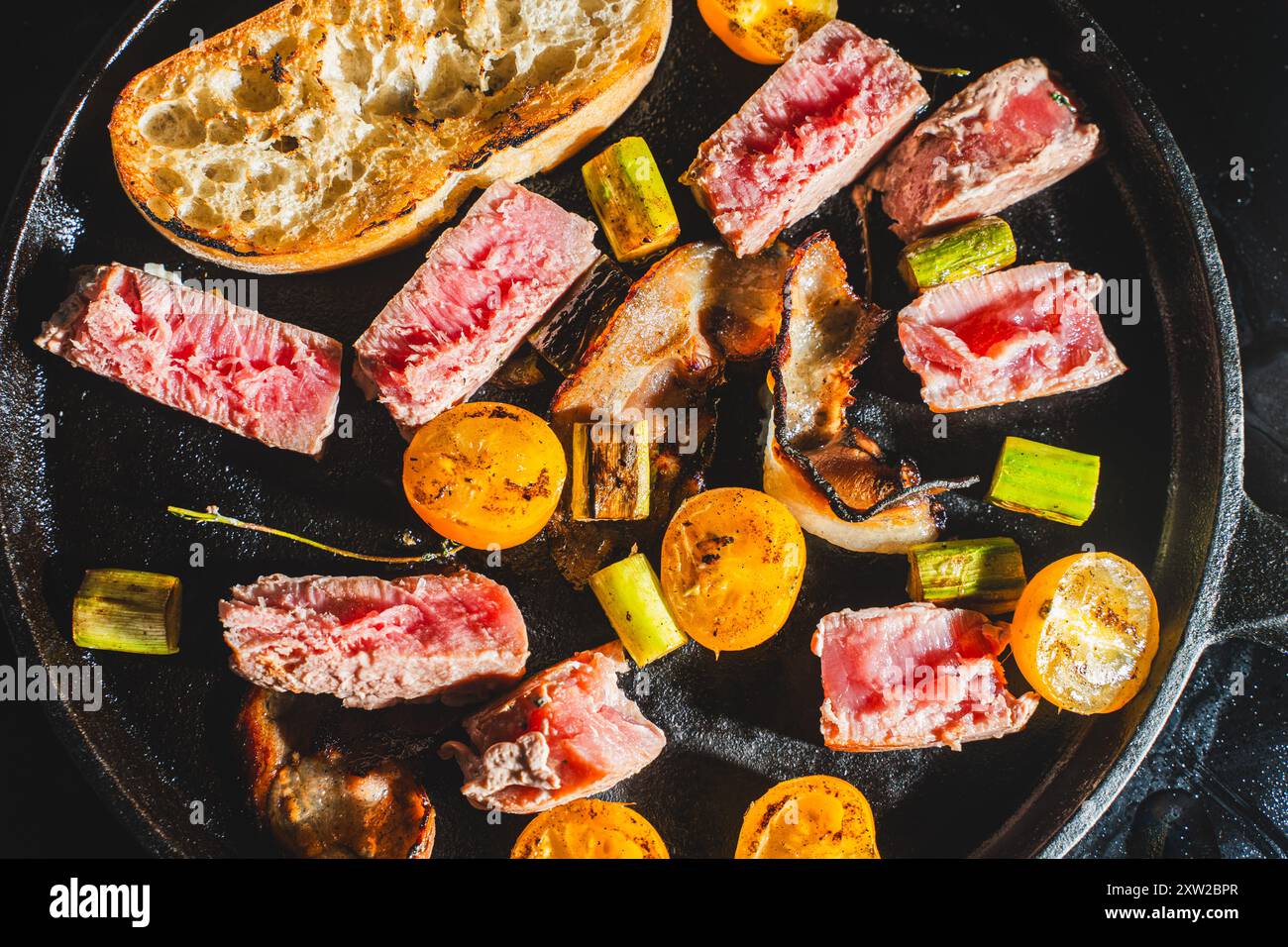 Thunfisch wird in einer gusseisernen Pfanne mit Kirschtomaten, Spargel, Speck und Toast gebraten. Hochwertige Fotos Stockfoto