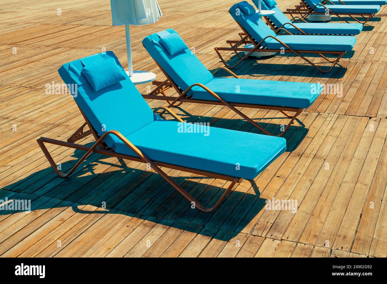 Gruppe von luxuriösen Sonnenliegen auf einem Holzsteg, die an einem heißen Sommertag auf Touristen warten. Reise-, Tourismus-, Freizeit- und Urlaubskonzept. Stockfoto