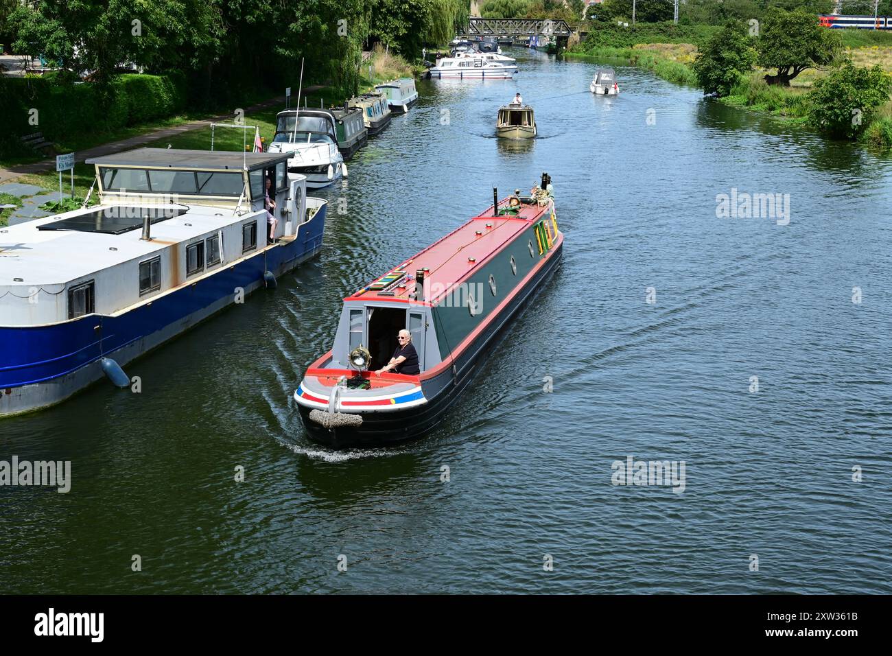 Schmales Boot, das an festgefahrenen Schiffen auf dem Fluss Great Ouse, Ely, Cambridgeshire, England, Großbritannien vorbeifährt Stockfoto
