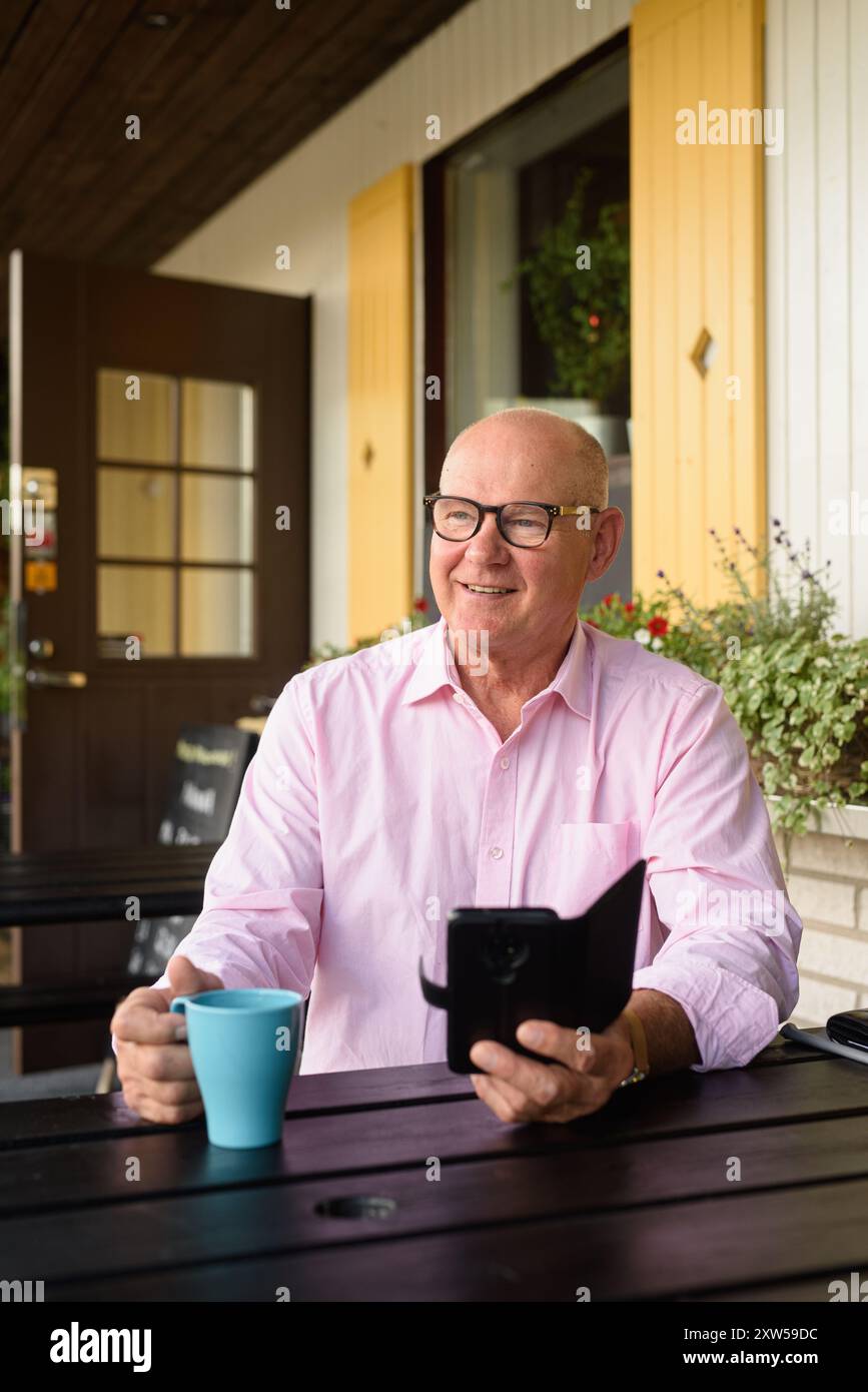 Glücklicher skandinavischer Senior Mann draußen im Restaurant mit Handy Stockfoto