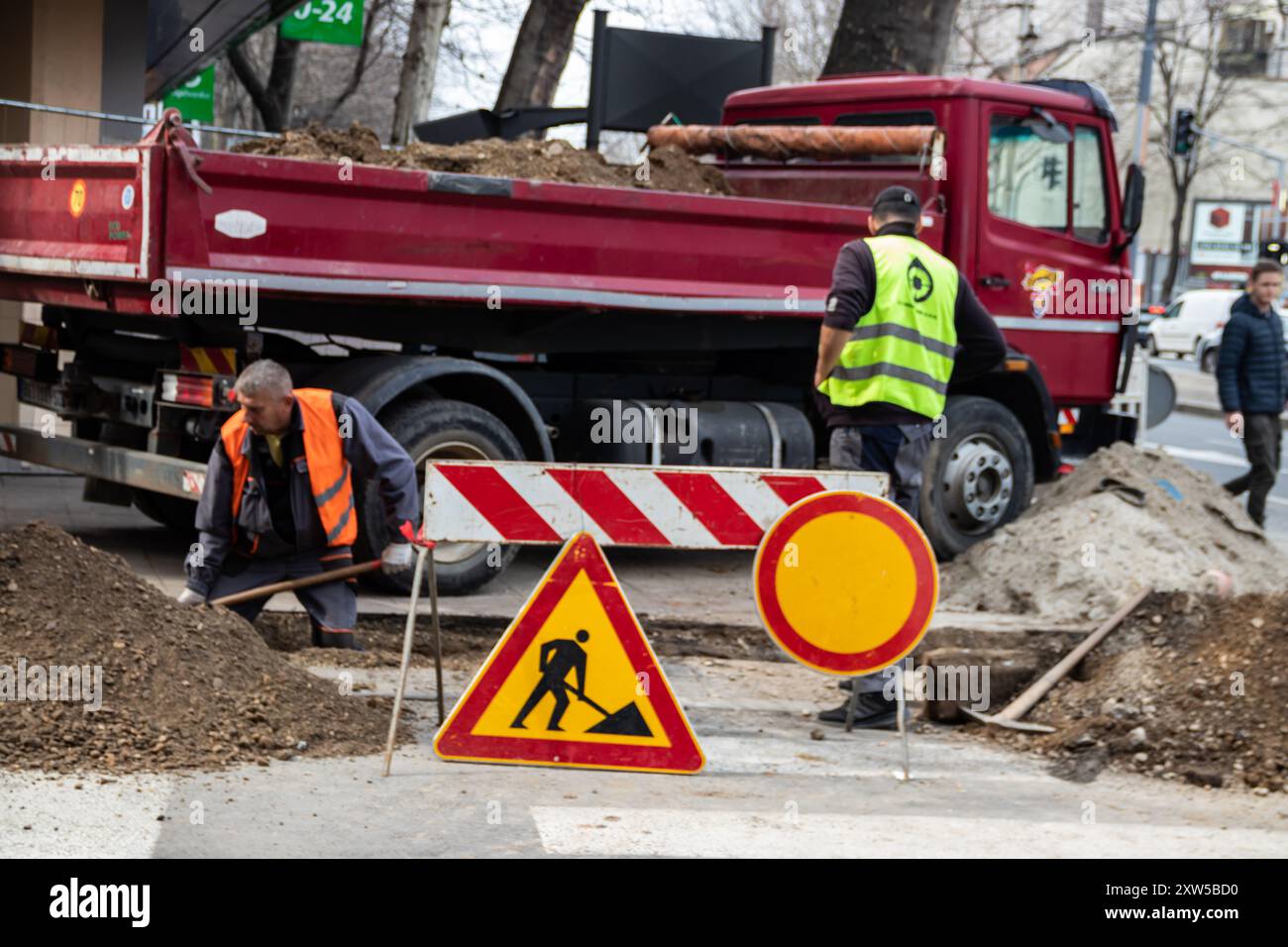en bei der Arbeit, in Schutzkleidung gekleidet, schwere Maschinen bedienen, während ein Arbeiter einen Graben aushebt, um Sicherheit und Teamarbeit auf der Baustelle zu gewährleisten Stockfoto