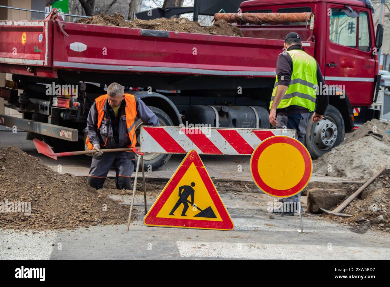 en bei der Arbeit, in Schutzkleidung gekleidet, schwere Maschinen bedienen, während ein Arbeiter einen Graben aushebt, um Sicherheit und Teamarbeit auf der Baustelle zu gewährleisten Stockfoto