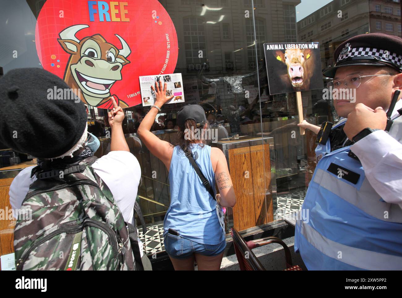 London, England, Großbritannien. August 2024. Demonstranten zeigen Kunden im Angus Steakhouse am Piccadilly Circus Schilder, während ein Polizist während der Demonstration beobachtet. Die Demonstranten treten für Gerechtigkeit, Respekt und Frieden für Tiere ein und gegen Ausbeutung und Unterdrückung. Sie versammeln sich, um jetzt Tierbefreiung zu fordern und in Solidarität mit allen Arten auf dem Planeten zu marschieren. (Kreditbild: © Martin Pope/ZUMA Press Wire) NUR REDAKTIONELLE VERWENDUNG! Nicht für kommerzielle ZWECKE! Stockfoto