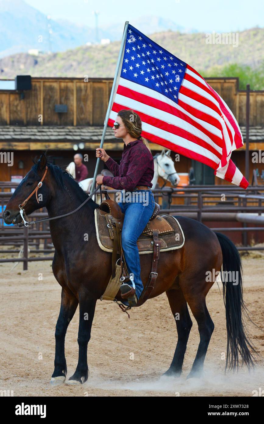 USA. ARIZONA. TUCSON. WEISSE HENGSTRANCH. FRAU AUF PFERD MIT AMERIKANISCHER FLAGGE WÄHREND EINES RODEOS. Stockfoto