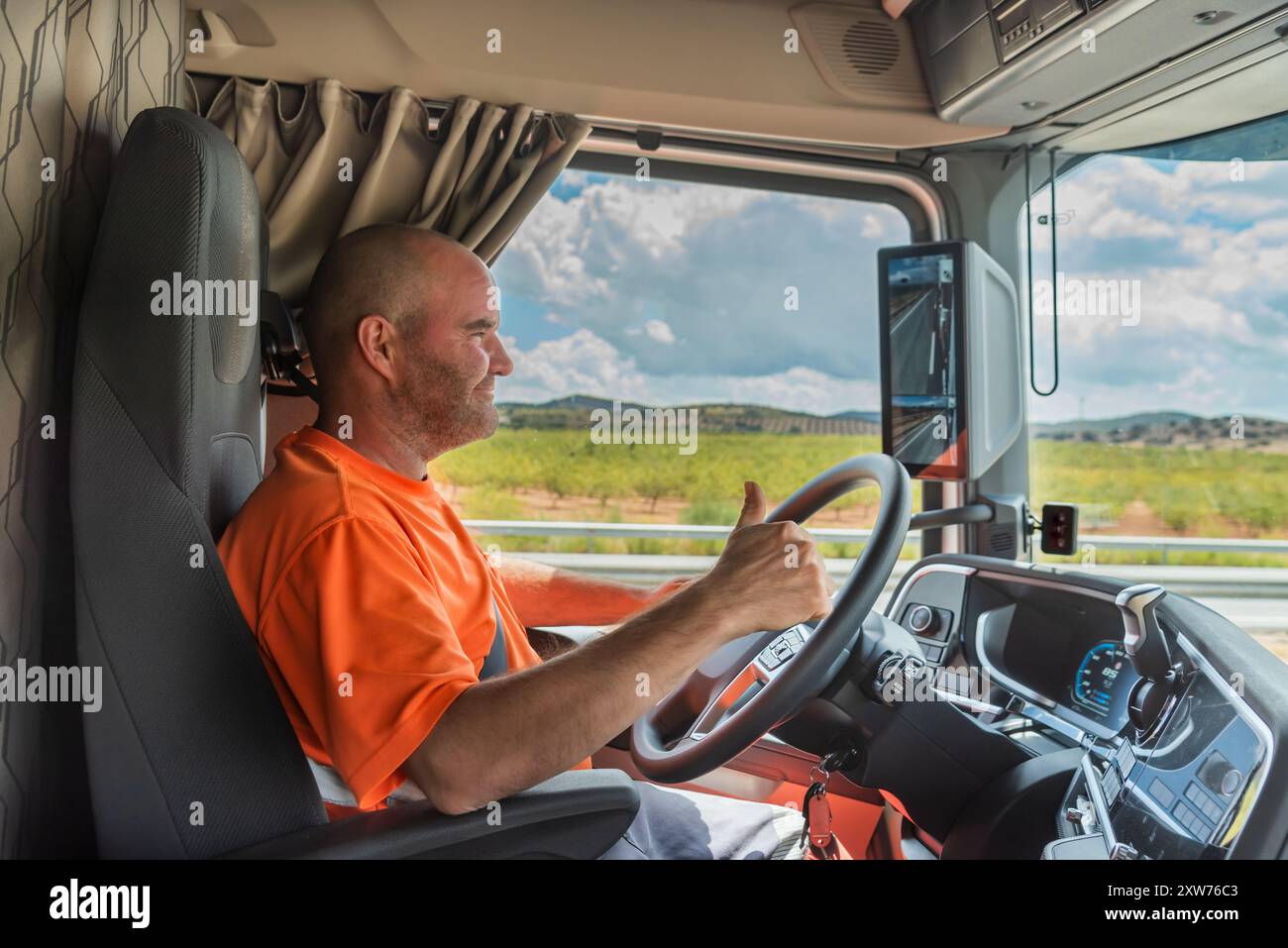 Glücklicher Trucker in der Kabine eines Lkws während der Fahrt mit dem Daumen nach oben im OK-Schild. Stockfoto
