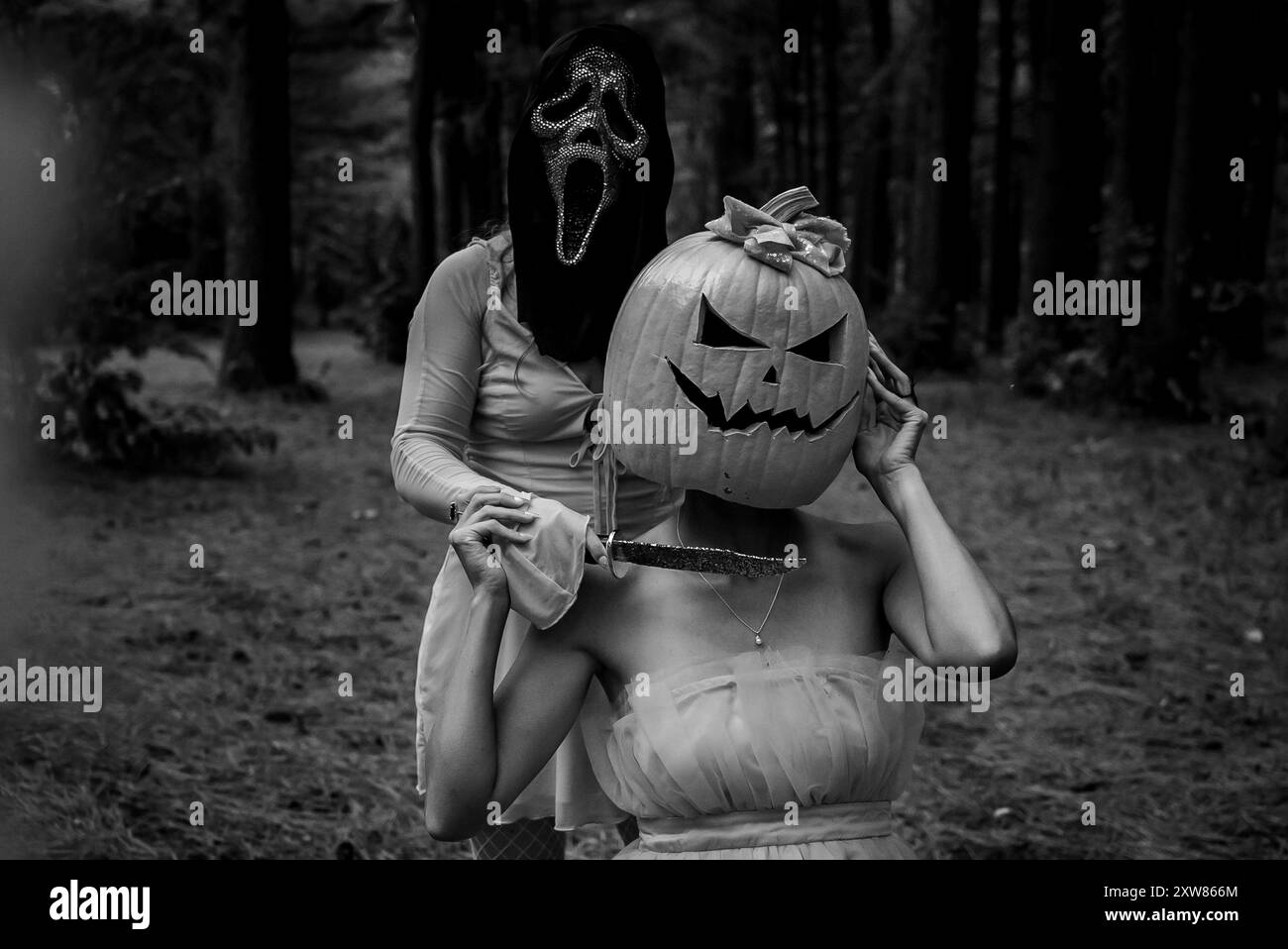 Zwei Frauen posieren mit Schreie- und Jack-o-Laternen-Kostümen im Hintergrund aus dunklem Holz Stockfoto