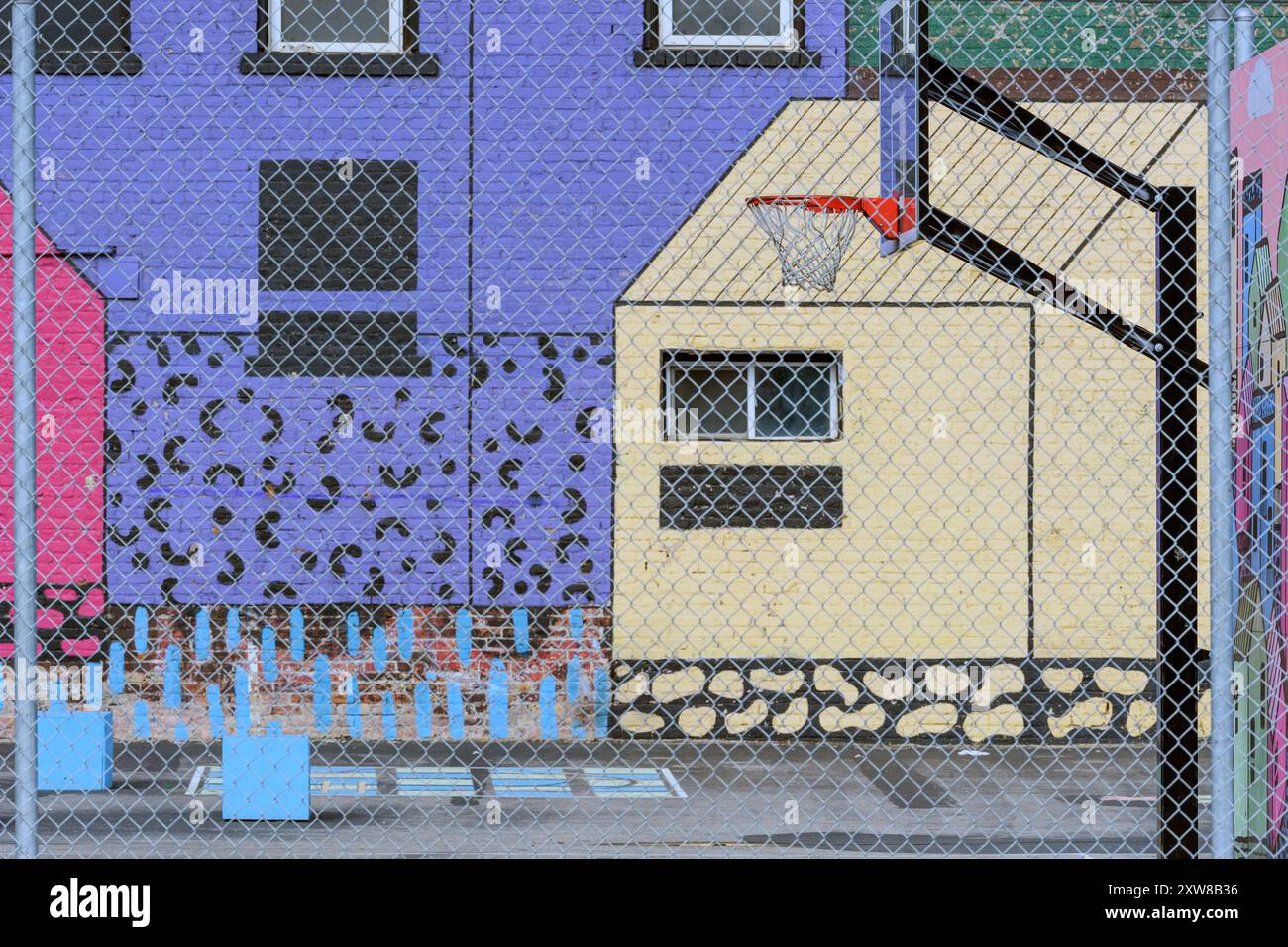 Farbenfrohes städtisches Street Art Wandgemälde an Gebäudewänden mit Basketballkorb und Spielplatz durch einen Maschendrahtzaun. Calgary Alberta Kanada. Stockfoto
