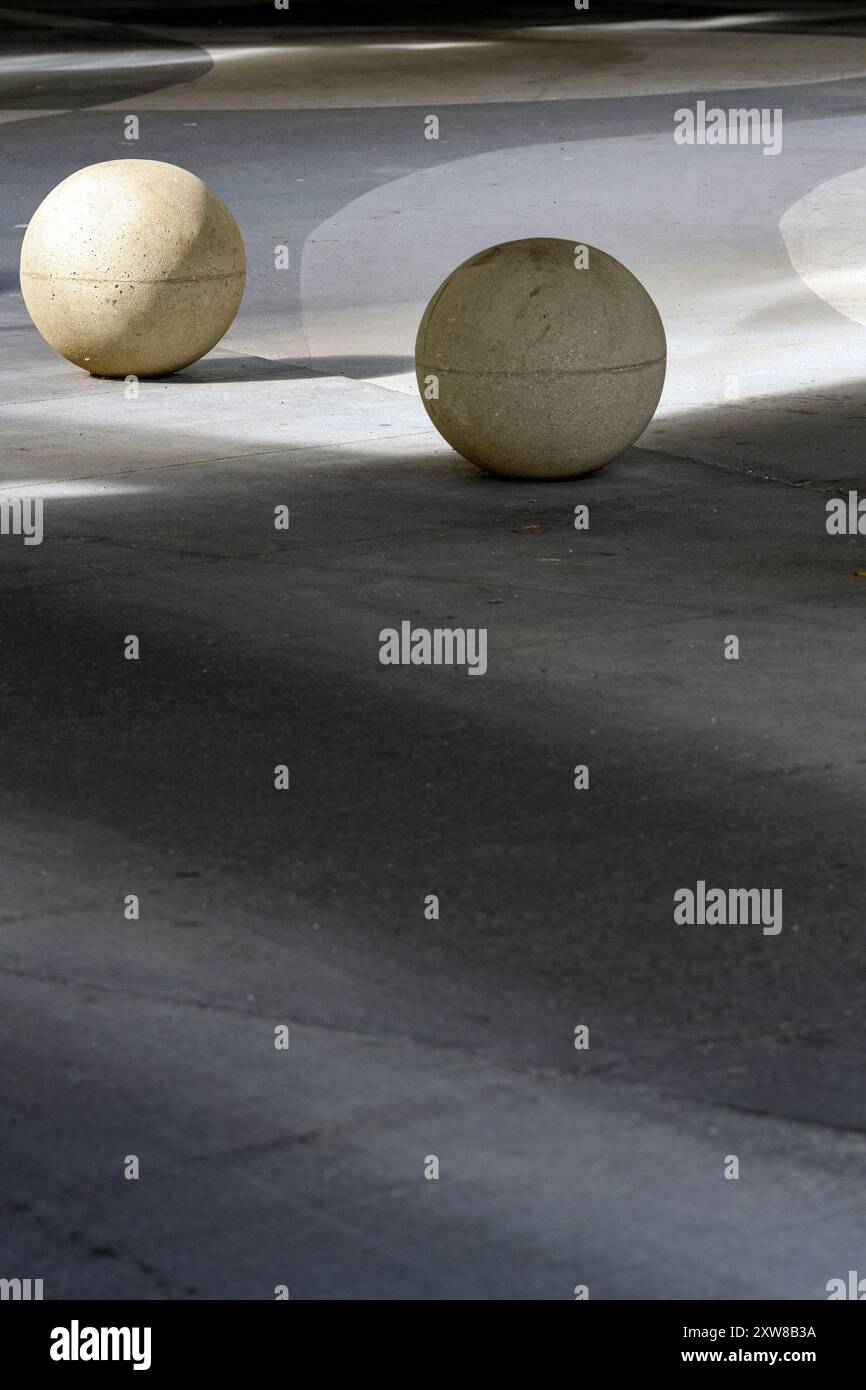 Zwei große kugelförmige Betonkonstruktionen, die an sonnigen Tagen Schatten auf eine gepflasterte Oberfläche werfen. Runde Betonbarriere. Stockfoto