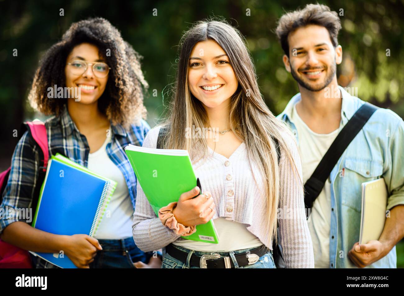 Drei glückliche Studenten stehen draußen auf dem Campus, halten Bücher und bereiten sich auf den Unterricht vor. Sie strahlen Spannung und Kameradschaft aus, während sie sich vorbereiten Stockfoto