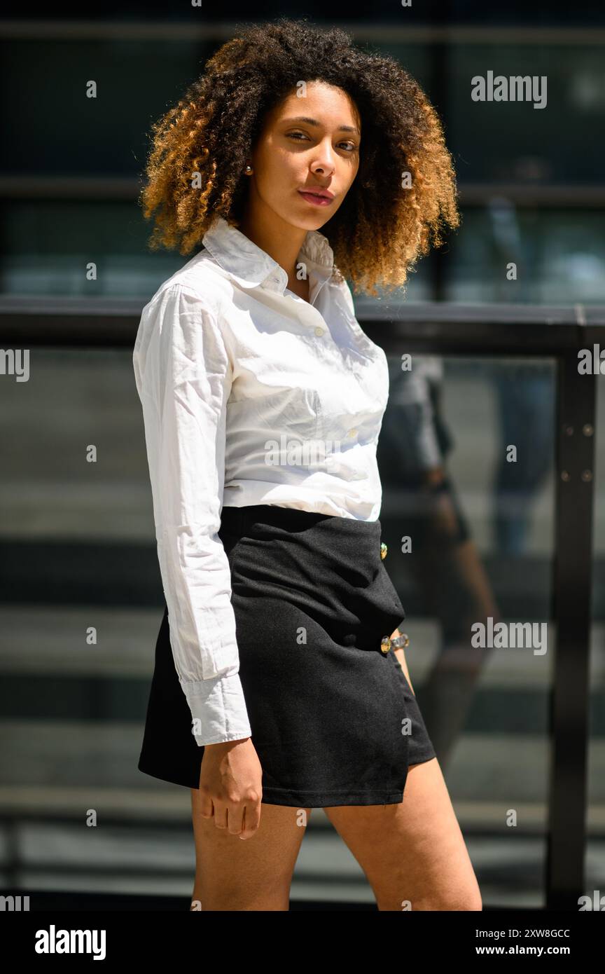 Stilvolle junge Managerin geht selbstbewusst zur Arbeit in die Stadt und strahlt Professionalität und Erfolg in ihrem eleganten Outfit aus. Ihr glückliches Lächeln strahlt Abschreckung aus Stockfoto